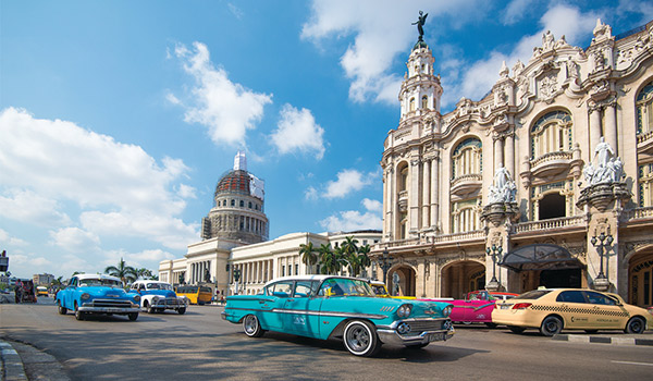 Classic American cars driving past historic buildings in Old Havana