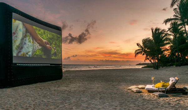 Écran gonflable sur lequel est joué un film sur la plage au coucher du soleil