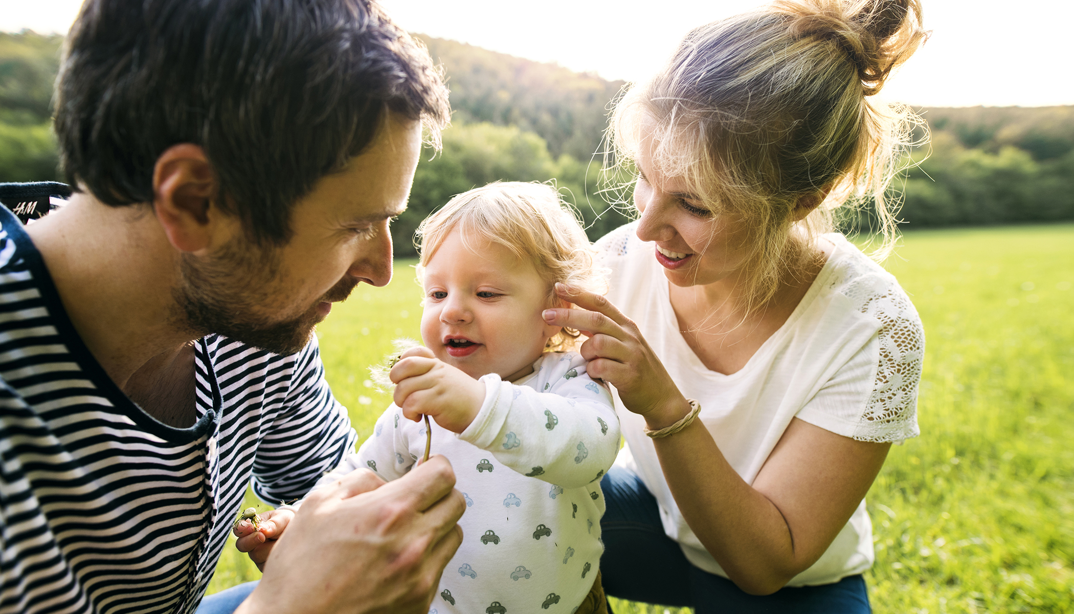 Visuel d'un couple avec son enfant assis dans l'herbe en été.