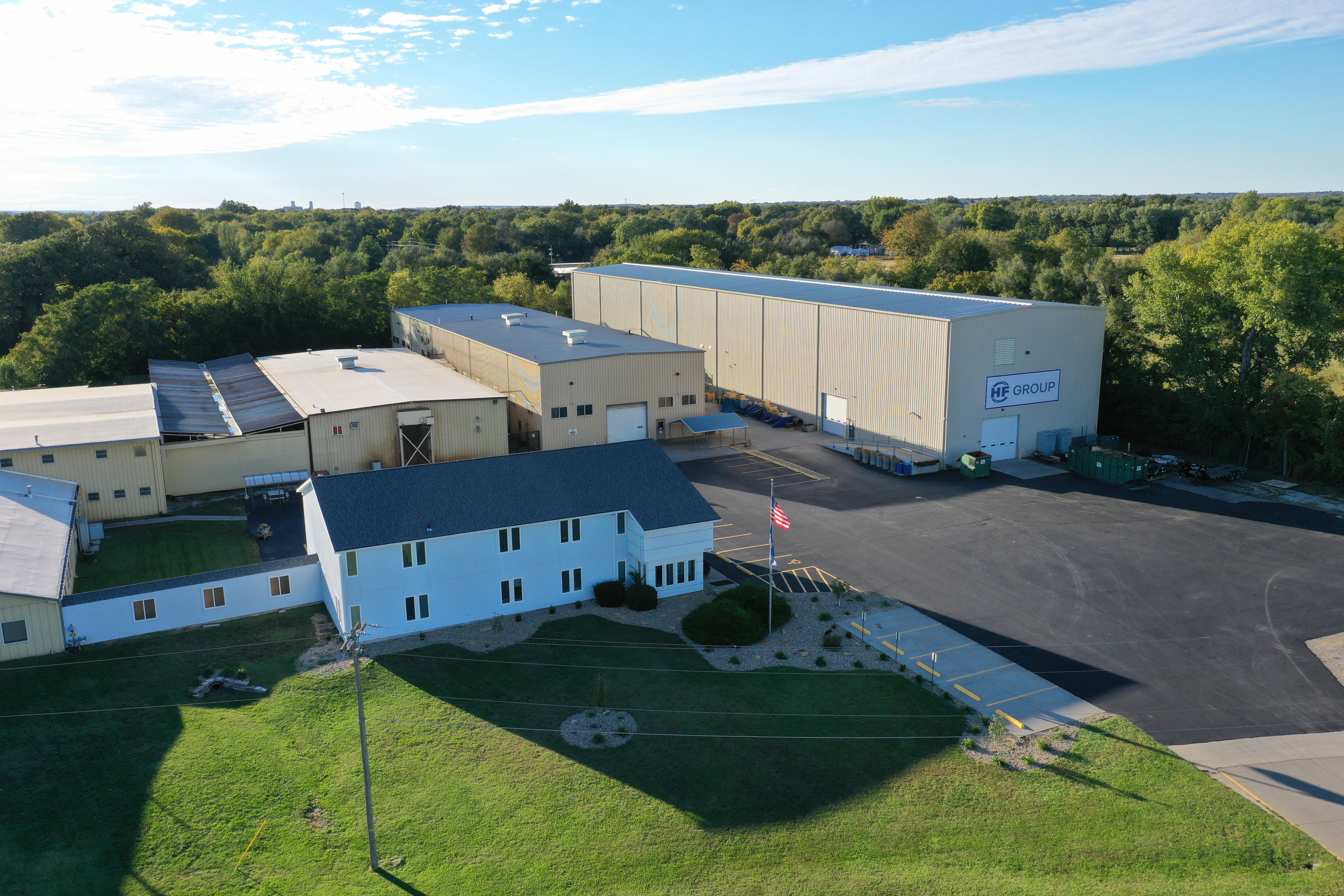 alt="Aerial view of the HF GROUP company building with adjacent production halls, surrounded by trees and green areas"