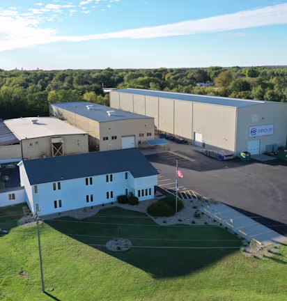 alt="Aerial view of the HF GROUP company building with adjacent production halls, surrounded by trees and green areas"