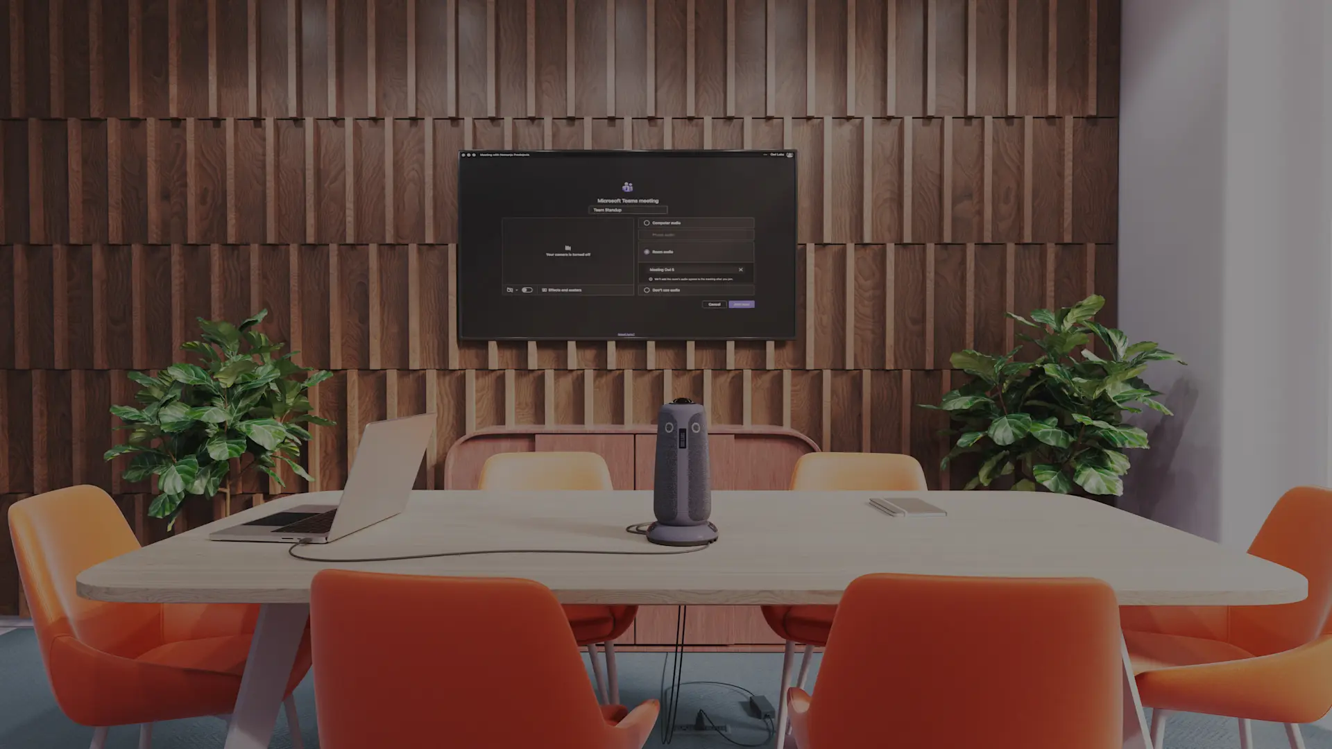 Meeting Owl 5 in an expanded conference room setting with a monitor on the wall behind it. The conference table is wide with empty, peach tone seats