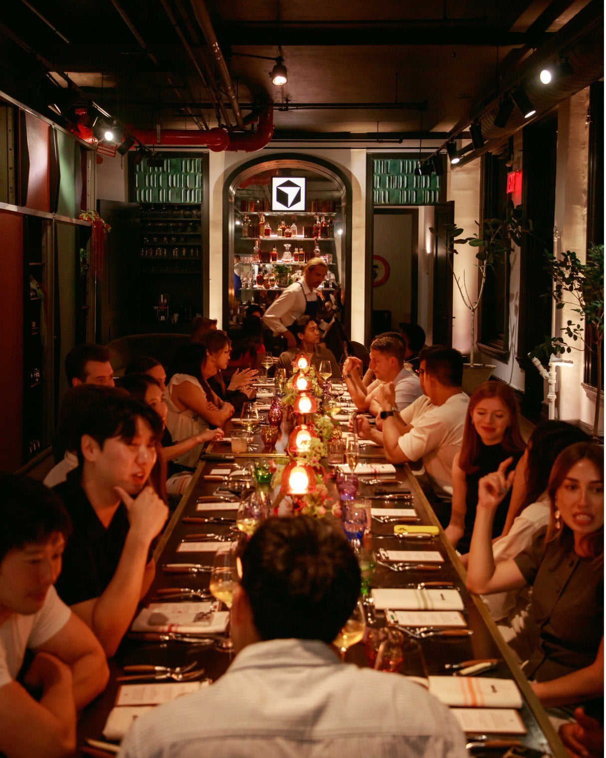 A social setting with a product identity. The communal table, warm lighting and brand presence are visible. The image does not establish the total guest count. User-supplied photo set [10].