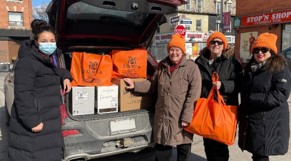 Zonta Club members besides a car trunk full of Orange Bags