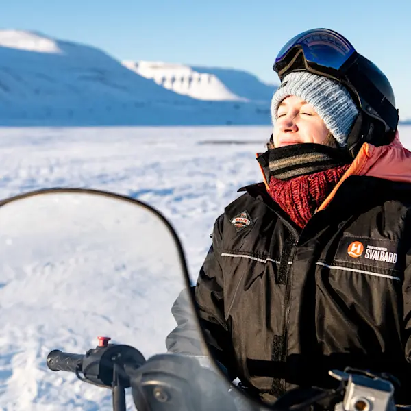 Happy guest on a snowmobile tour smiling in the sun