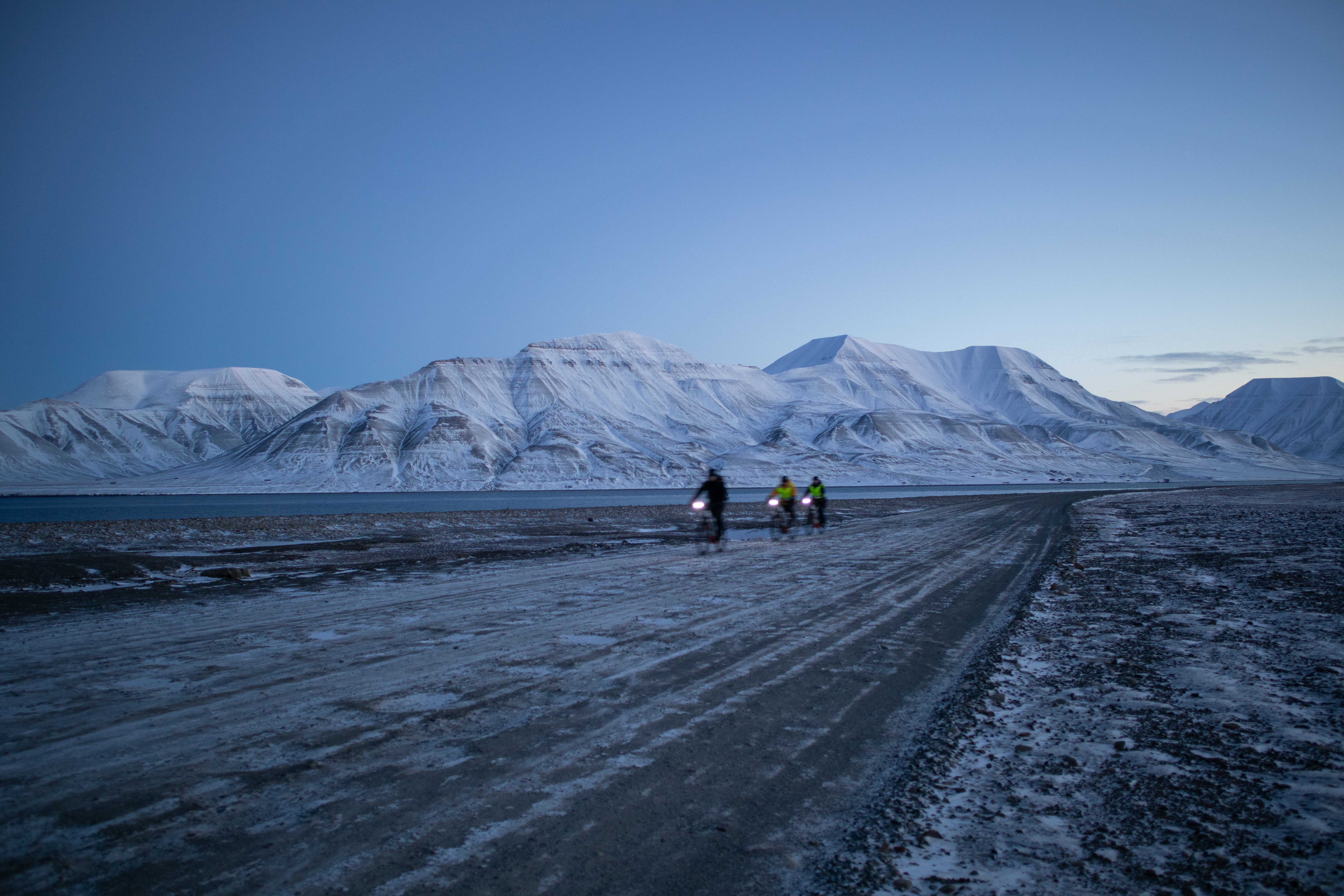 Guests cycling along the road against the backdrop of snowcapped mountains. Photo Credit: Eveline Lunde / Hurtigruten Svalbard