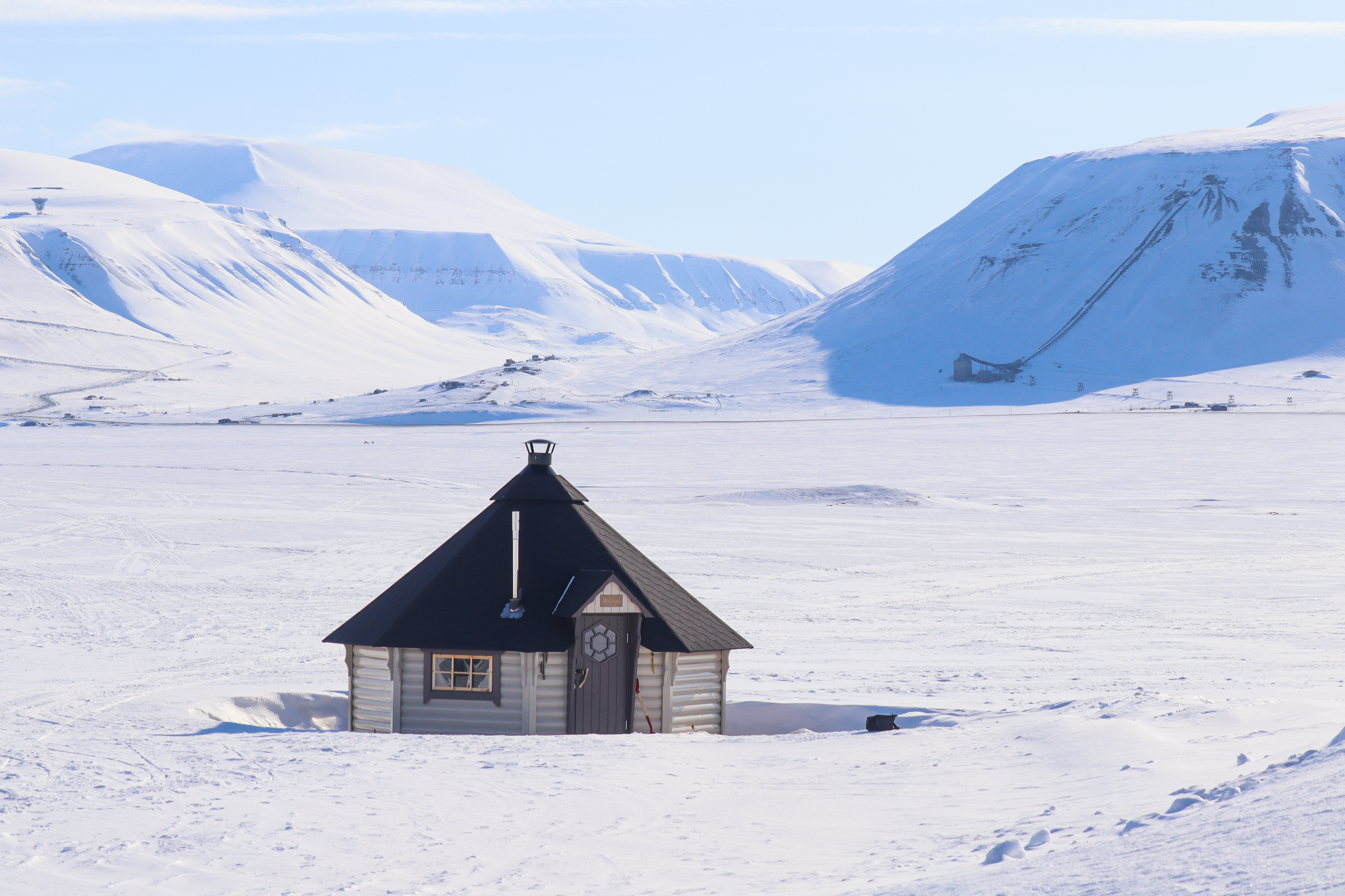 Cabin surrounded by snowcapped mountains during the Sunny Winter in Svalbard. Photo Credit: Eveline Lunde / Hurtigruten Svalbard