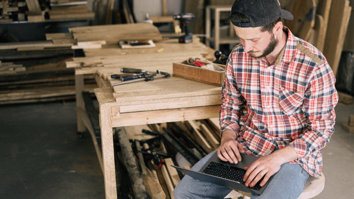 Man using laptop while sitting at woodworking desk.