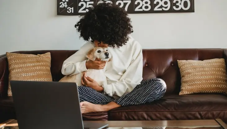 Woman snuggling dog in front of laptop on couch