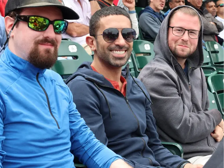 Three colleagues sitting together outdoors at a sporting event