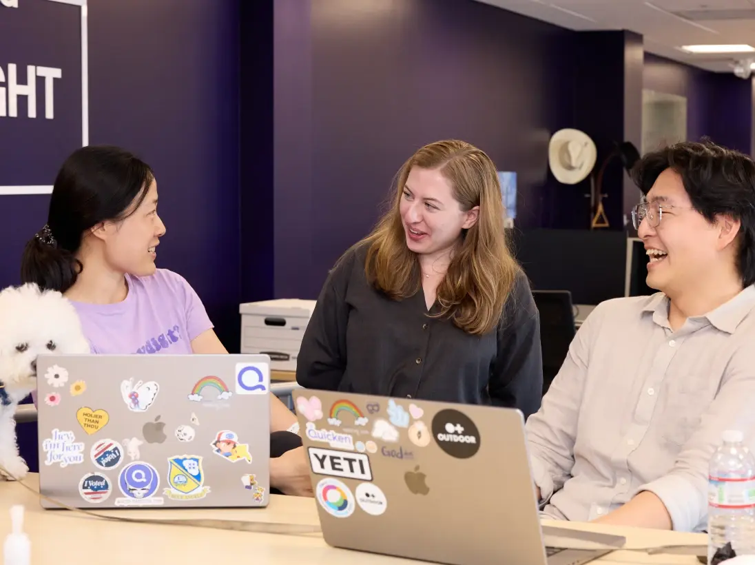 Three colleagues collaborating at a desk with laptops in the office