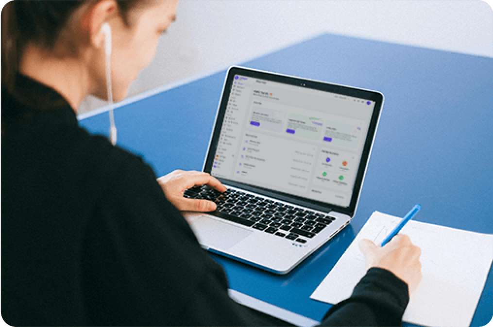 Women is working with paper,pen and laptop. While wearing a headphones.