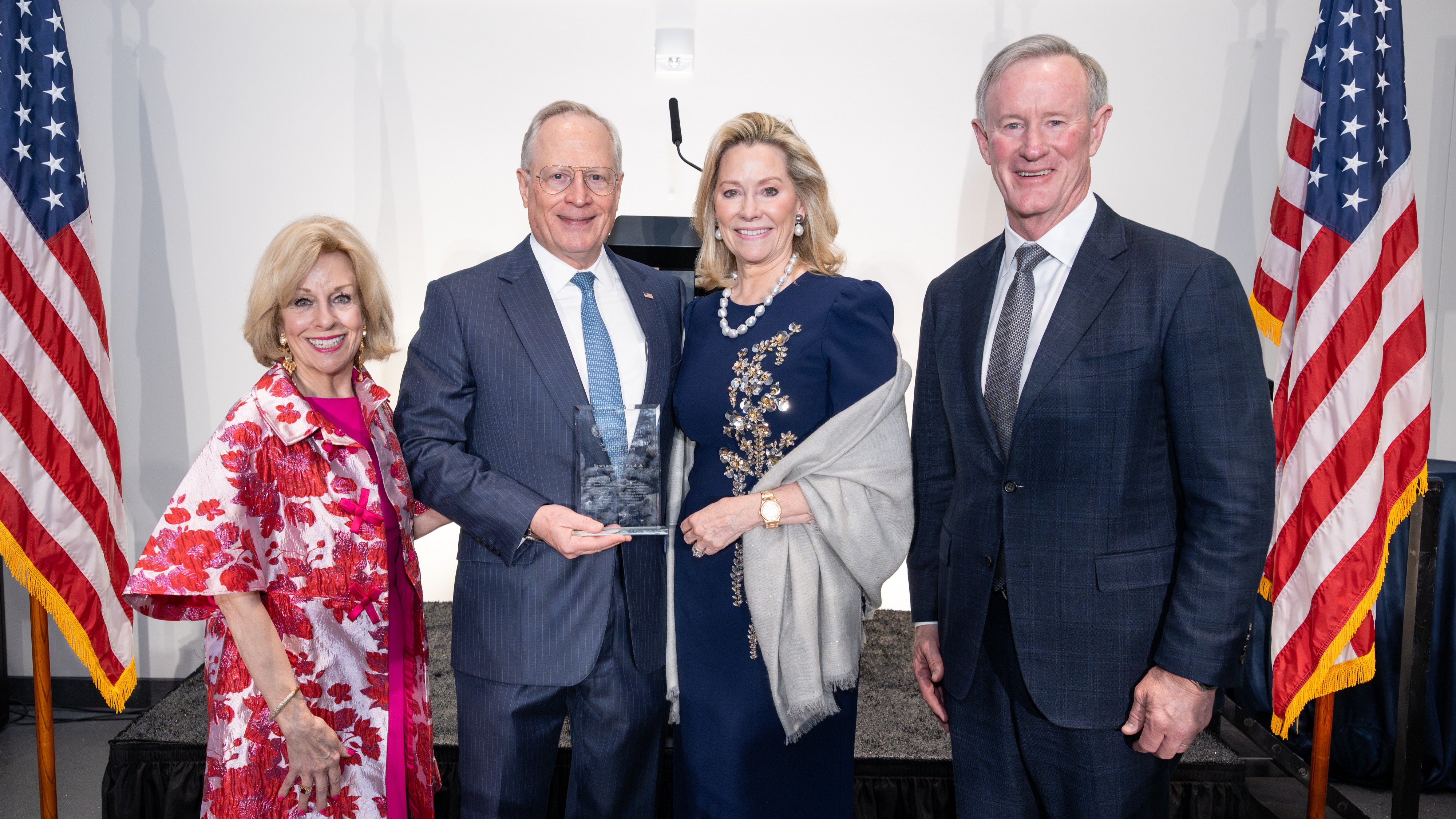 Sandi Chapman, PhD, stands alongside 2026 Legacy Award recipients Ross Perot, Jr. and Sarah Perot, and past Legacy Award recipient Admiral William McRaven (ret.), flanked by patriotic flags at the Museum of Honor Museum in Arlington, Texas.