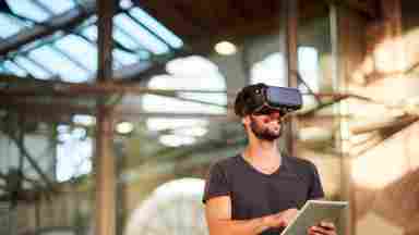 A happy man is wearing a virtual reality headset while holding a tablet. iStock: 1139534054