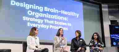 Dr. Krystal Sexton speaks during a BrainHealth Week panel discussion at a Center for BrainHealth in Dallas, Texas, in front of a large LCD screen that reads "Designing Brain-Healthy Organizations: Strategy That Scales to Everyday Practice."