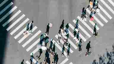 An aerial view of a crowd using the crosswalks in a large 4-way intersection.