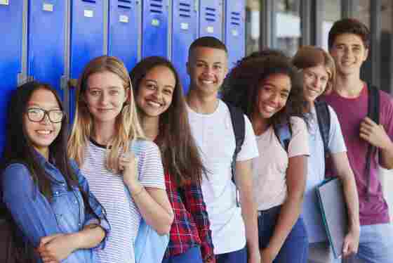 A group of teenage students are smiling while leaning against lockers. 