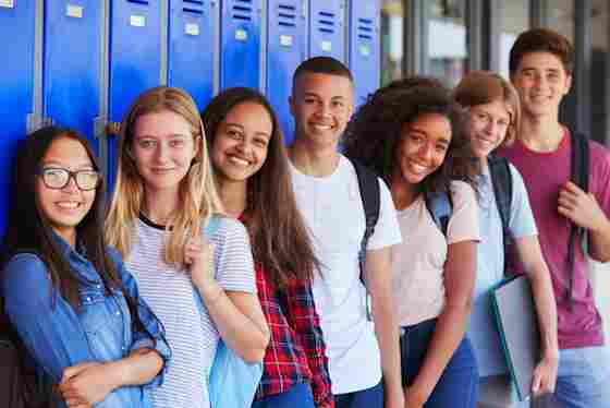 A group of teenage students are smiling while leaning against lockers.