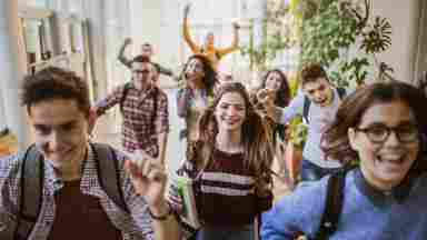 Large group of high school students running to class through a hallway. Focus is on a happy student looking at the camera.