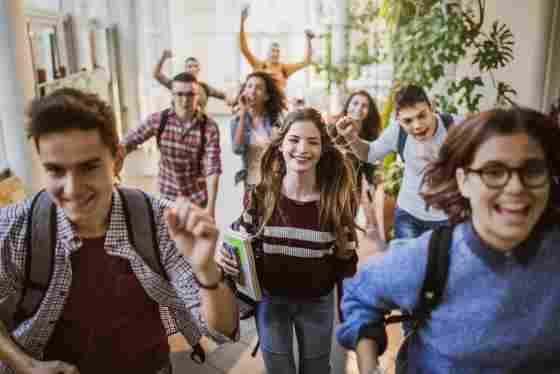 Large group of high school students running to class through a hallway. Focus is on a happy student looking at the camera.