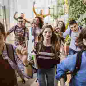 Large group of high school students running to class through a hallway. Focus is on a happy student looking at the camera.