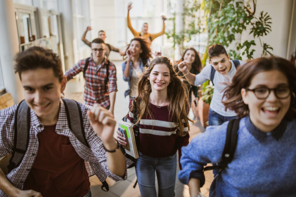 Large group of high school students running to class through a hallway. Focus is on happy student looking at camera. Youth. Teens. Happy. 