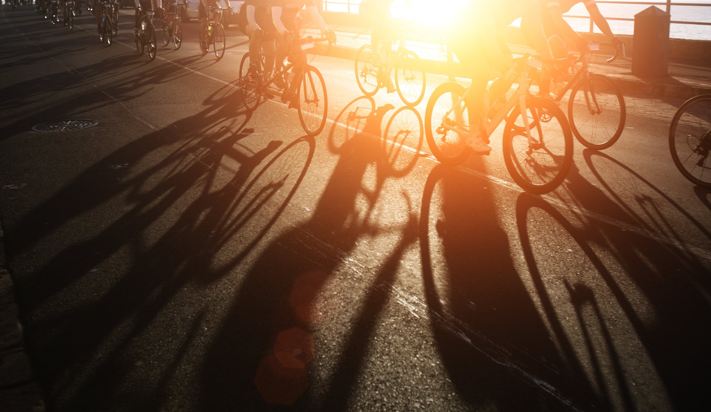 Cyclists ride in critical mass across a sunlit bridge at dawn.