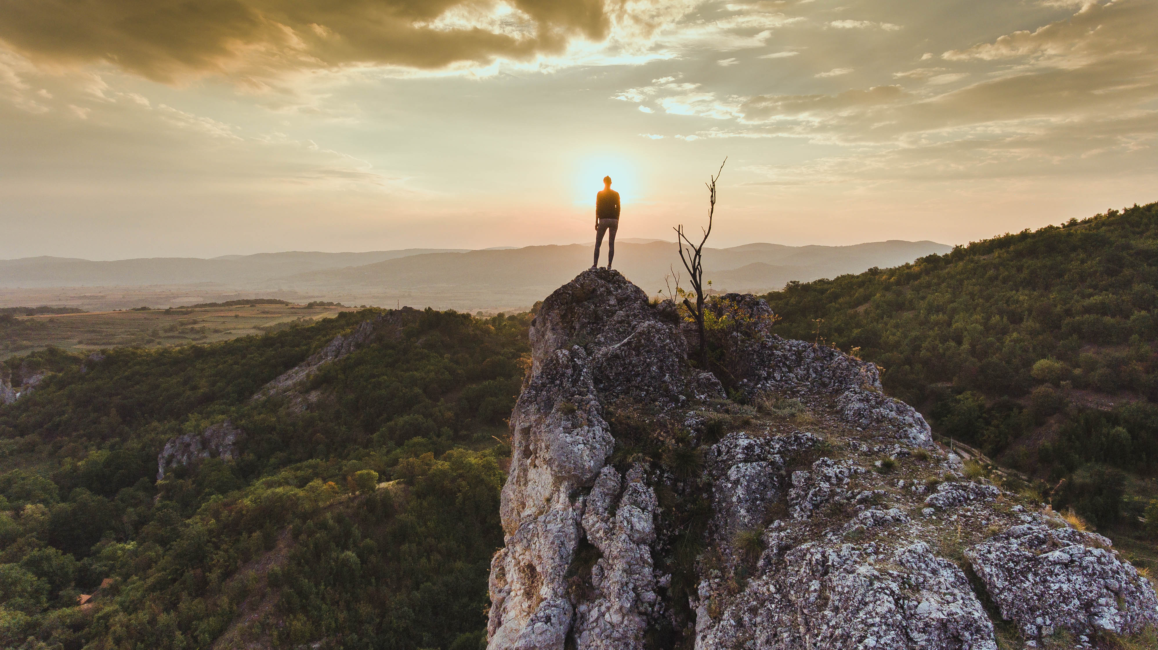 A silhouette of a hiker on a mountain overlooking a sunset.