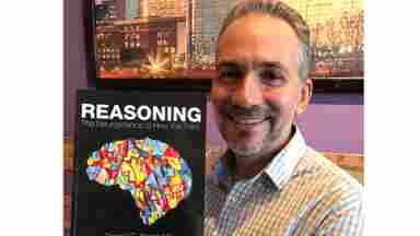 Dr. Dan Krawczyk smiles and poses with his textbook, Reasoning: The Neuroscience of How We Think.