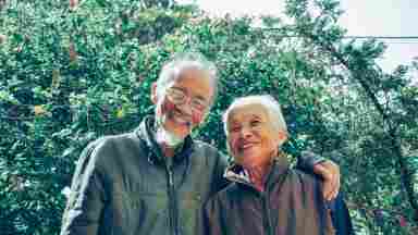 Elderly couple smiling, outdoors on a beautiful day.