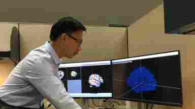 Dr. Daniel Yang, assistant research professor at the George Washington University and Children’s National Health System, stands looking at scans of brains on a computer monitor.