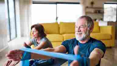 A happy senior couple with elastic bands indoors at home, doing exercise on the floor. 