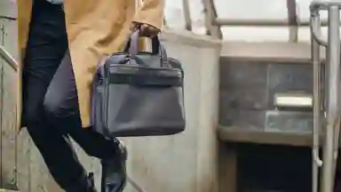 A man of color in an yellow trench coat walking out of a subway station with a book bag