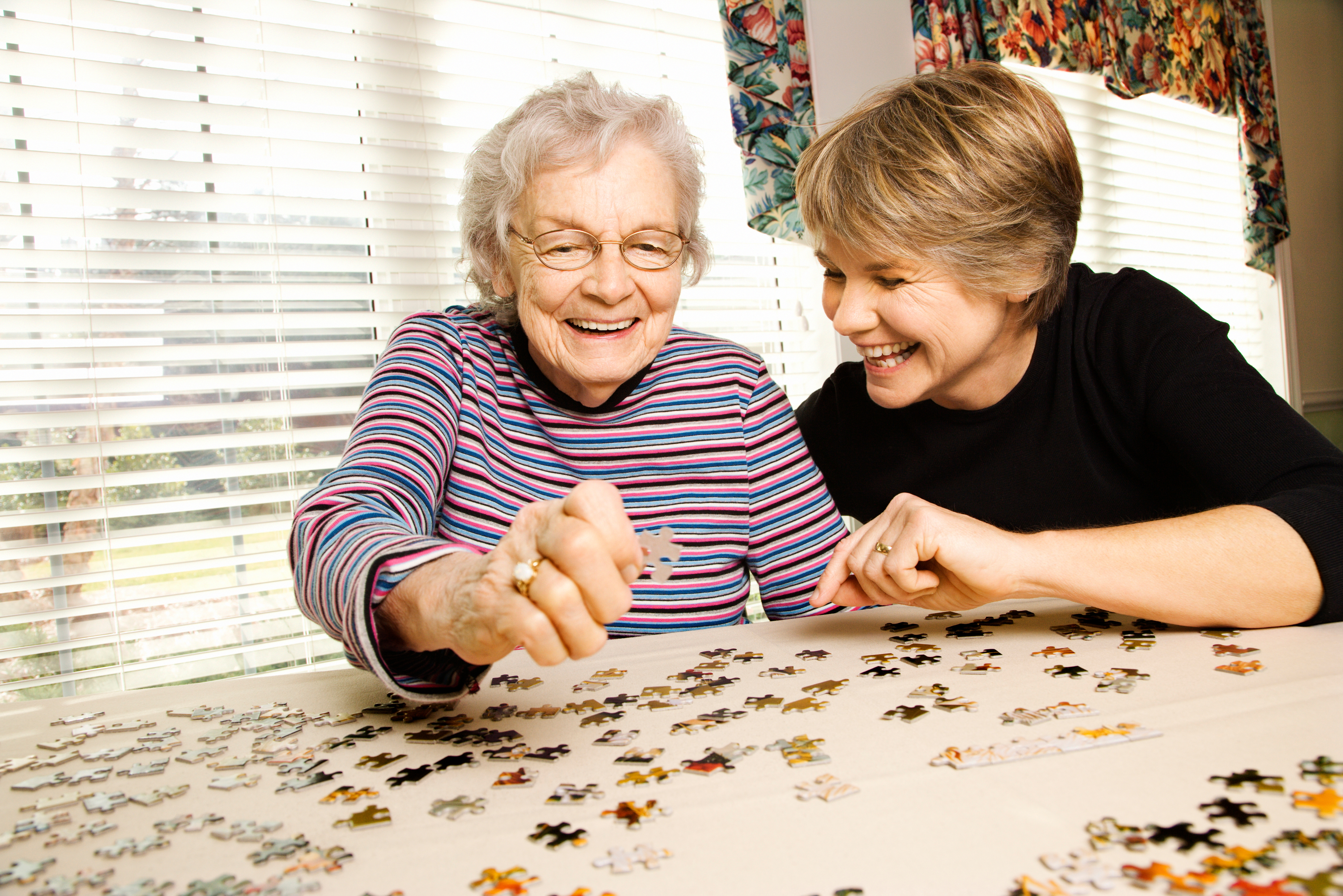 Two women, one older and one younger, solve a puzzle together while smiling.