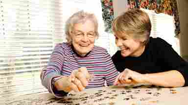 Two women, one older and one younger, solve a puzzle together while smiling.