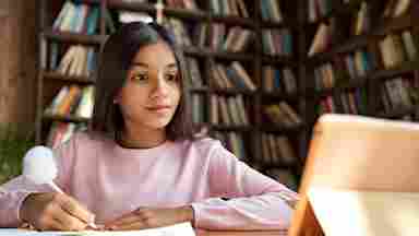 A young female student is studying while looking at the tablet. Child. Kid. Youth.