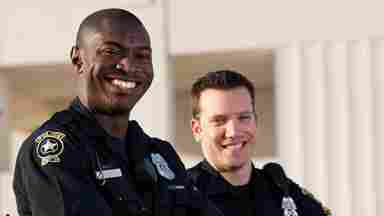 Two male police officers stand smiling with their arms folded.