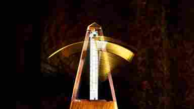 A wooden metronome in motion against a dark background.