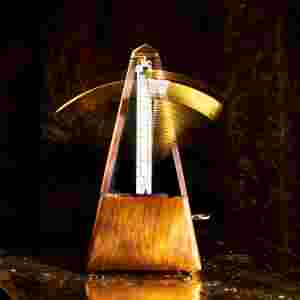 A wooden metronome in motion against a dark background.