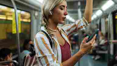 A collage-aged woman wears earbuds and calmly listens to music on the subway.