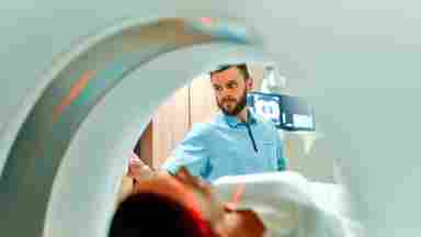 A man giving a woman a MRI scan. Brain imaging. iStock-1311263197