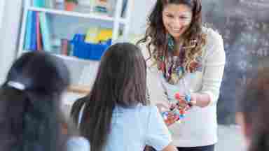 A happy female teacher chats with a student about a molecular model.  