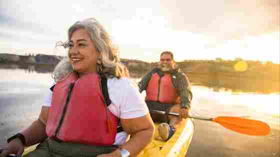 A mature Latino couple happily kayak together and watch a glowing sunset.