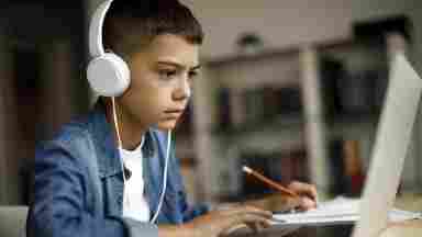 A young boy sitting at a laptop computer and wearing headphones as he studies or does homework.