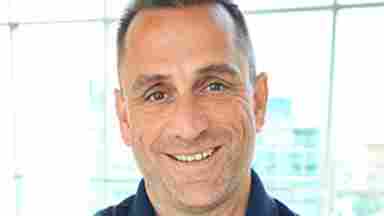 A headshot of Robert L. Rennaker II, Ph.D. who is wearing a navy blue shirt and standing in a brightly lit room.