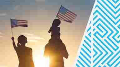 Silhouettes of two parents and a young child, holding American flags as the sun sets.