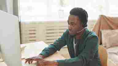 Young man wearing headset and working on computer from home.