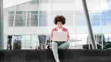 Businesswoman with afro hair wearing formal clothes sitting outdoors in business area and using her computer.
