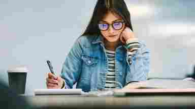  A focused female student with glasses is studying in a school or library setting. Youth. Teen.