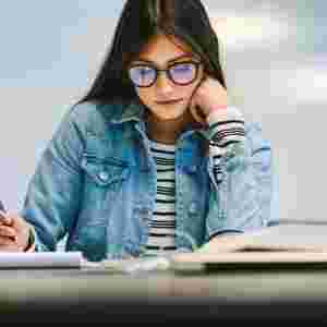  A focused female student with glasses is studying in a school or library setting. Youth. Teen.